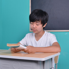 Smart Asian student reading book in classroom