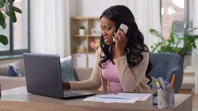 remote job, technology and people concept - stressed african american young woman with laptop computer and papers working at home office and calling on smartphone