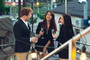 Corporate celebrating in the warm light of the lamps in summer evening, young friends, colleagues look happy, talk, have fun. Holidays, weekend, business and finance, friendship concept. Teambuilding.