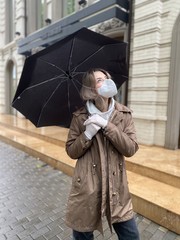 young woman with umbrella. beautiful stylish girl in a protective flu mask and gloves, stands on the street with umbrella
