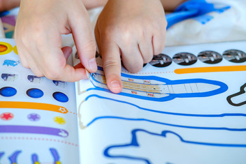 Child’s hand, Kid’s hand is sticking rocket sticker on space education activity book. Space...