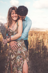 Happy woman and man, he is hugging her from behind in a meadow, woman holding corsage flower