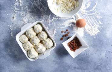 Cooking process. Preparation. Cottage cheese in a white bowl, raisins, eggs and flour on a light grey background. Flatlay, top view. Background image, copy space