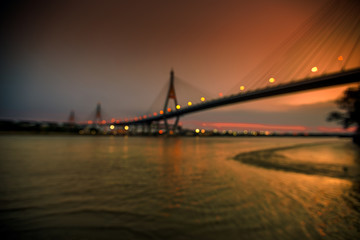Obraz premium The blurred background of the twilight evening by the river, the natural color changes, the bridge over the river (Bhumibol Bridge) is one of the major transportation bridges in Bangkok, Thailand