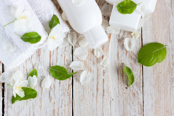 White rolled up towels and bottles with cosmetics on a light wooden background. Flatlay. Spa and beauty treatment concept. Copy space for text.