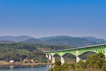 Railroad on a bridge over ria de Arousa and wind turbines on the mountains in a sunny day