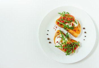 delicious poached eggs on crispy slices of wheat bread with slices of tomato, arugula, spices and black pepper on a white plate on a white background
