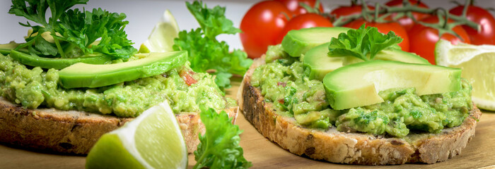 Slice of bread with guacamole made from avocado, tomato, lime, poarsley and garlic - close up  - banner design