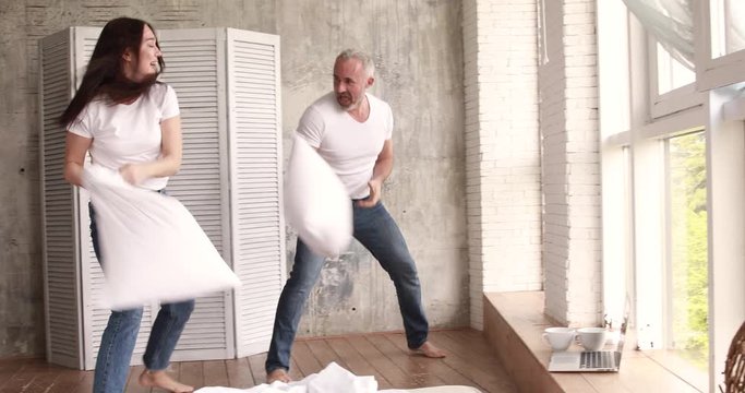 Husband and wife fight pillows and laugh. They are home on self-isolation.