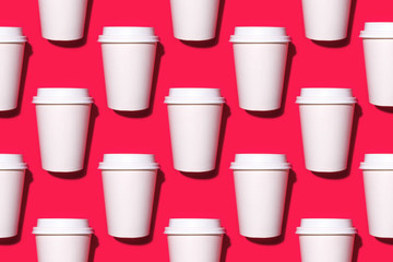 Pattern of disposable coffee cups on a red background. Flat lay.