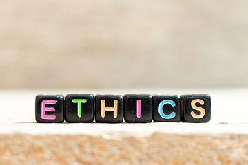 Black bead with color letter in word ethics on wood background