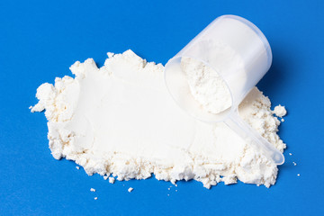 Scattered protein powder and measuring spoon on blue background, a copy of the spree