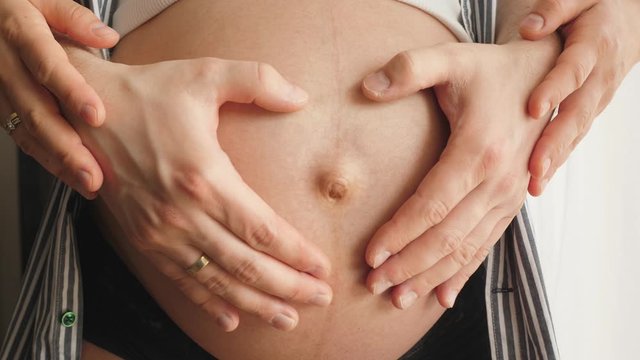 parents make making a heart shape with their hands on pregnant belly