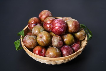 Fresh plums in a woven bamboo basket against a black background