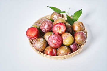 Fresh plum fruits in woven bamboo baskets on a white background
