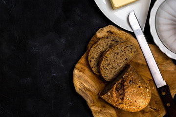 Sliced rye bread with knife and butter. Dark background. Top view