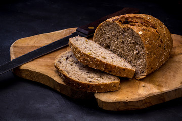 Loaf of bread with knife on wooden board. Dark background