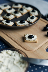 Plate with crackers with soft cheese and olives on a blue polka dot tablecloth.