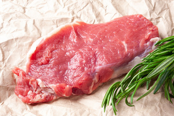 Raw meat. Slice of fresh raw meat with rosemary on paper. Preparing meat for a barbecue.