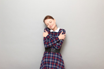 Portrait of cute happy young blond woman embracing herself and smiling