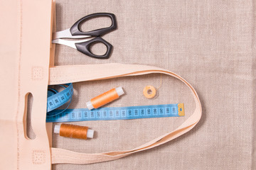 scissors, measuring tape and several spools of thread in an eco bag on linen fabric, top view, copy location, sewing fabric shopping bag