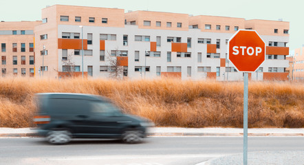 Panning of black van with city in the background, with dry field and clear sky and STOP sign