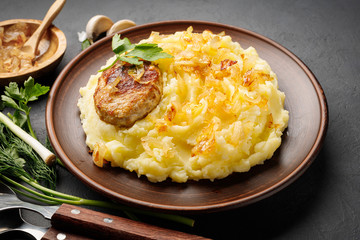 Mashed potatoes, boiled puree with fried onions and cutlet in a brown plate.