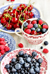Red and blue berries - forest blueberries, blueberries, raspberries, cherries in a  dish with a red and blue pattern.  Summer berries. Soft focus