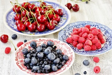 Red and blue berries - forest blueberries, blueberries, raspberries, cherries in a  dish with a red and blue pattern.  Summer berries. Soft focus