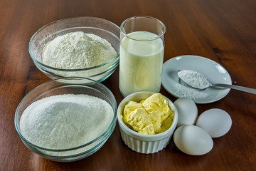 Basic ingredients for making cake, flour, sugar, milk, eggs, butter and yeast on wooden table. Ingredients for homemade cake