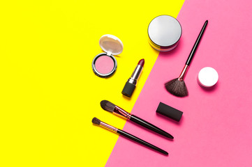 Professional makeup brushes, powder, eyeshadow, blush, lipstick on yellow pink background flat lay top view copy space. Beauty product women's accessory fashion. Different brushes. Cosmetic makeup Set
