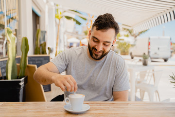 hombre joven moreno feliz y sonriente mientras toma café