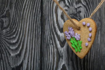 Gingerbread decorated with glaze. Made in the shape of a heart. Hanging on a rope. Against the background of brushed pine boards.