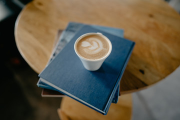 taza blanca de café sobre libros de lectura en mesa de madera