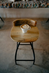 taza de café blanca con dibujo de corazón encima de una silla de madera