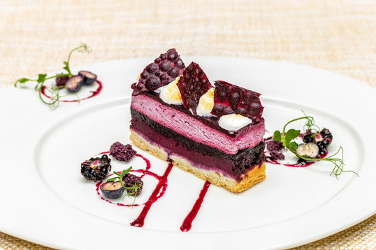 Black currant cake with meringue and sauce on a white plate
