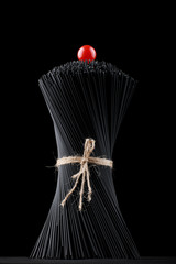Black spaghetti pasta is raw on a black background with fresh tomatoes.