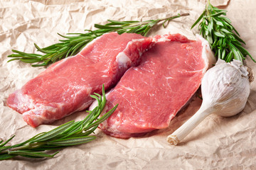 Raw meat and garlic. Two slices of fresh raw meat, garlic and rosemary on paper. Preparing meat for a barbecue.