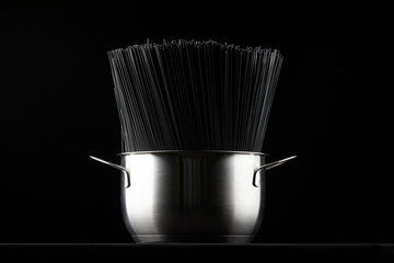 Black spaghetti pasta in a saucepan on a black background.