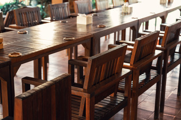 Preparation of wooden dining table and chairs with flower in vase and napkin at restaurant