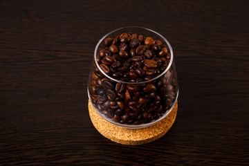 Fototapeta na wymiar Glass goblet with coffee beans is isolated on a wooden background on a cork wood stand. Close-up.