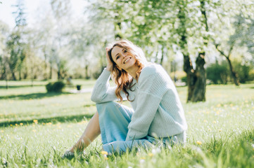 Fototapeta premium The beautiful girl the blonde holds with eyes closed in hand the blossoming apple-tree branch with white flowers in a garden in sunshine. Spring apple trees in blossom. woman among spring blossom.