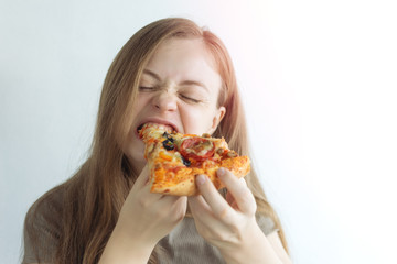 Young caucasian woman girl hungrily biting eating a slice of pizza with a funny face