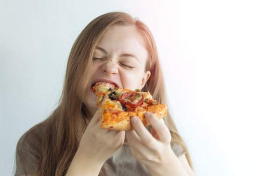 Young caucasian woman girl hungrily biting eating a slice of pizza with a funny face