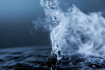 Boiling water splash with steam on dark blue background closeup