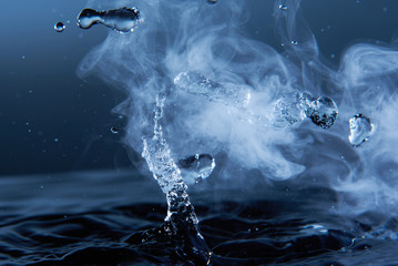 Boiling water splash with steam on dark blue background closeup