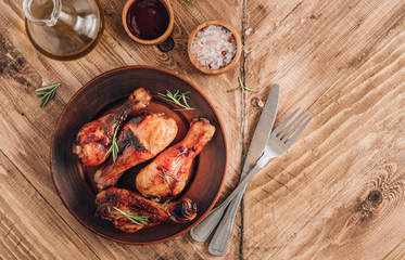 Chicken legs on brown plate with sauce and rosemary on wooden rustic background. Top view