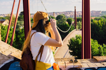 Girl with cap, sunglasses, golden sports jacket and leather backpack facing the river at dawn .Looking with goggles. Lifestyle concept