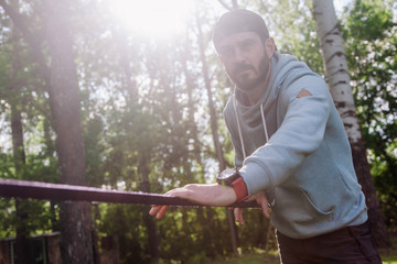 portrait of a young, athletic, bearded guy in a blue hoodie near slackline