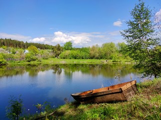 fishing boat on the lake on a sunny day against a blue sky with clouds and countryside on the opposite shore